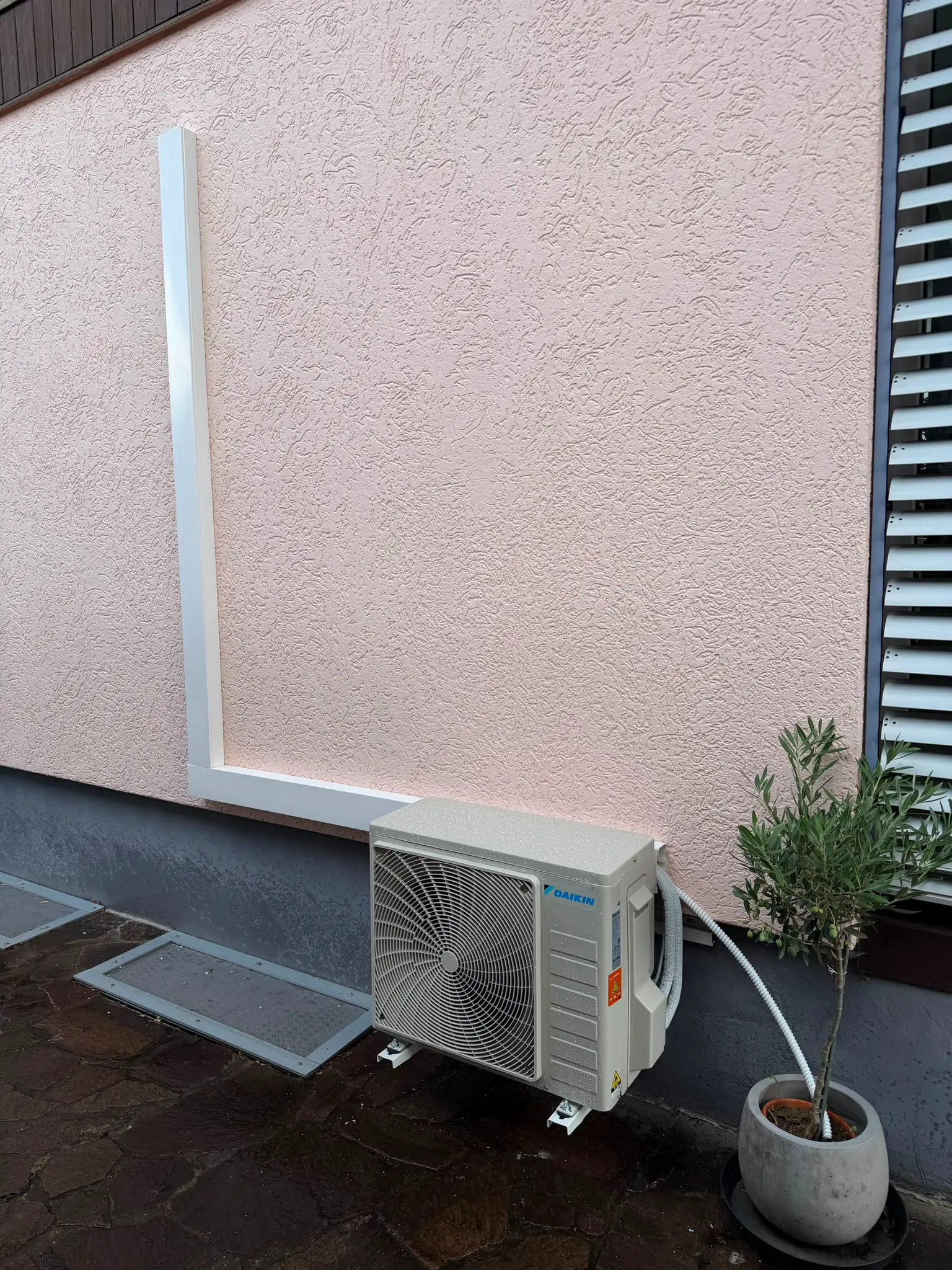 Außengerät von Daikin auf einer Terrasse; der weiße Leitungskanal führt im rechten Winkel an der Wand entlang.