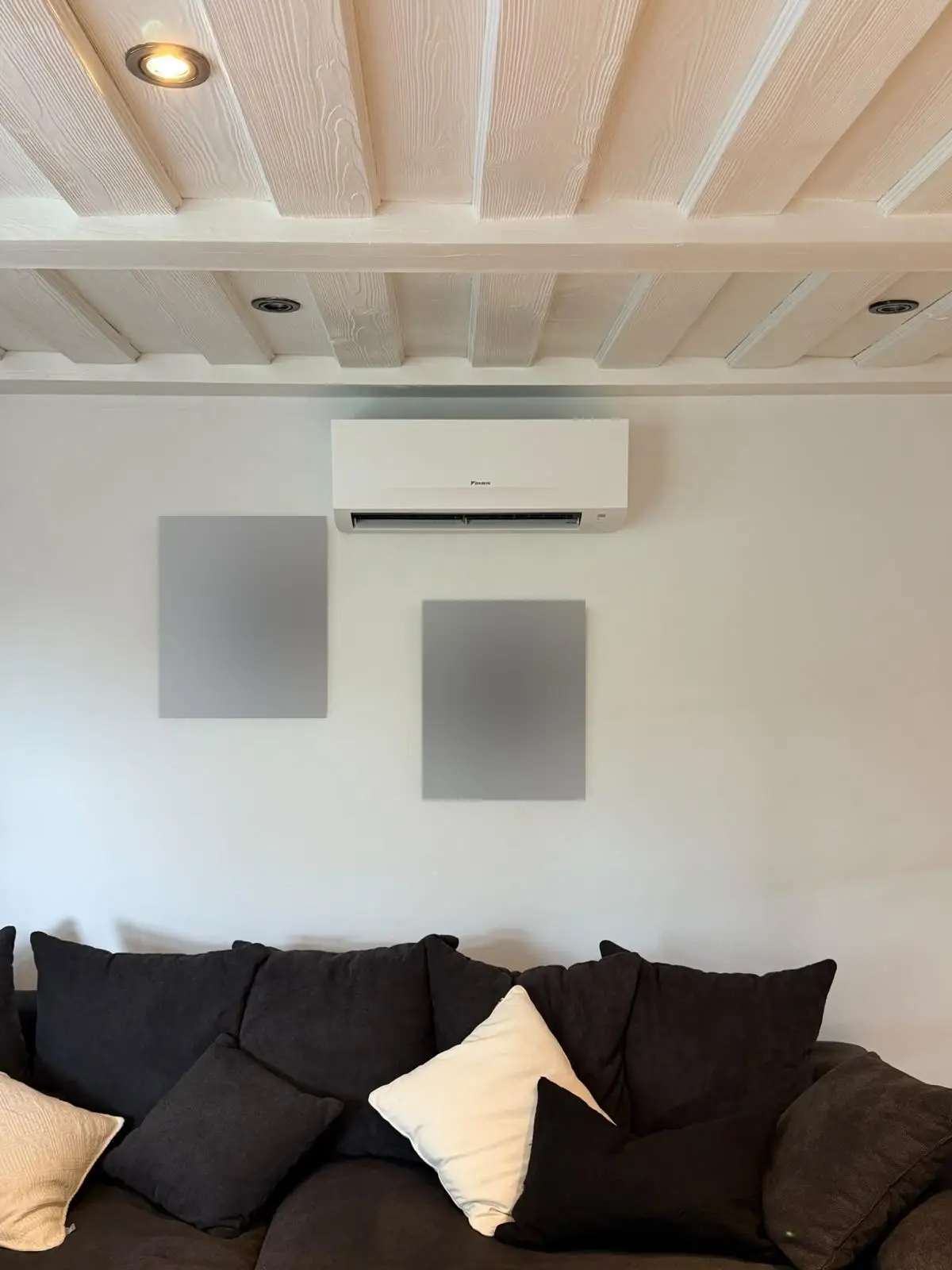Innengerät von Daikin an einer hellen Wohnzimmerwand unter einer weiß gestrichenen Balkendecke, darunter ein Sofa.