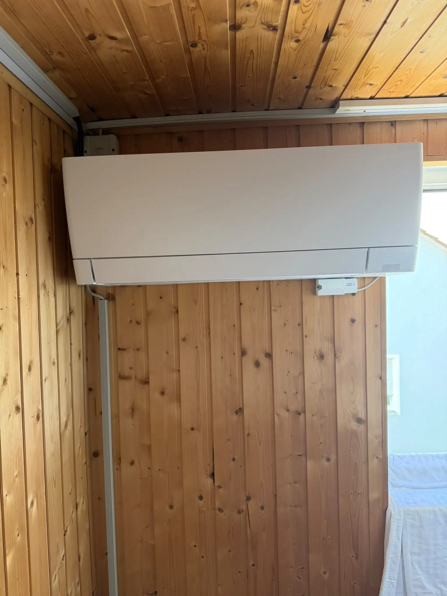 Innengerät von Mitsubishi Electric an einer Holzvertäfelung; der weiße Leitungskanal führt senkrecht nach unten.