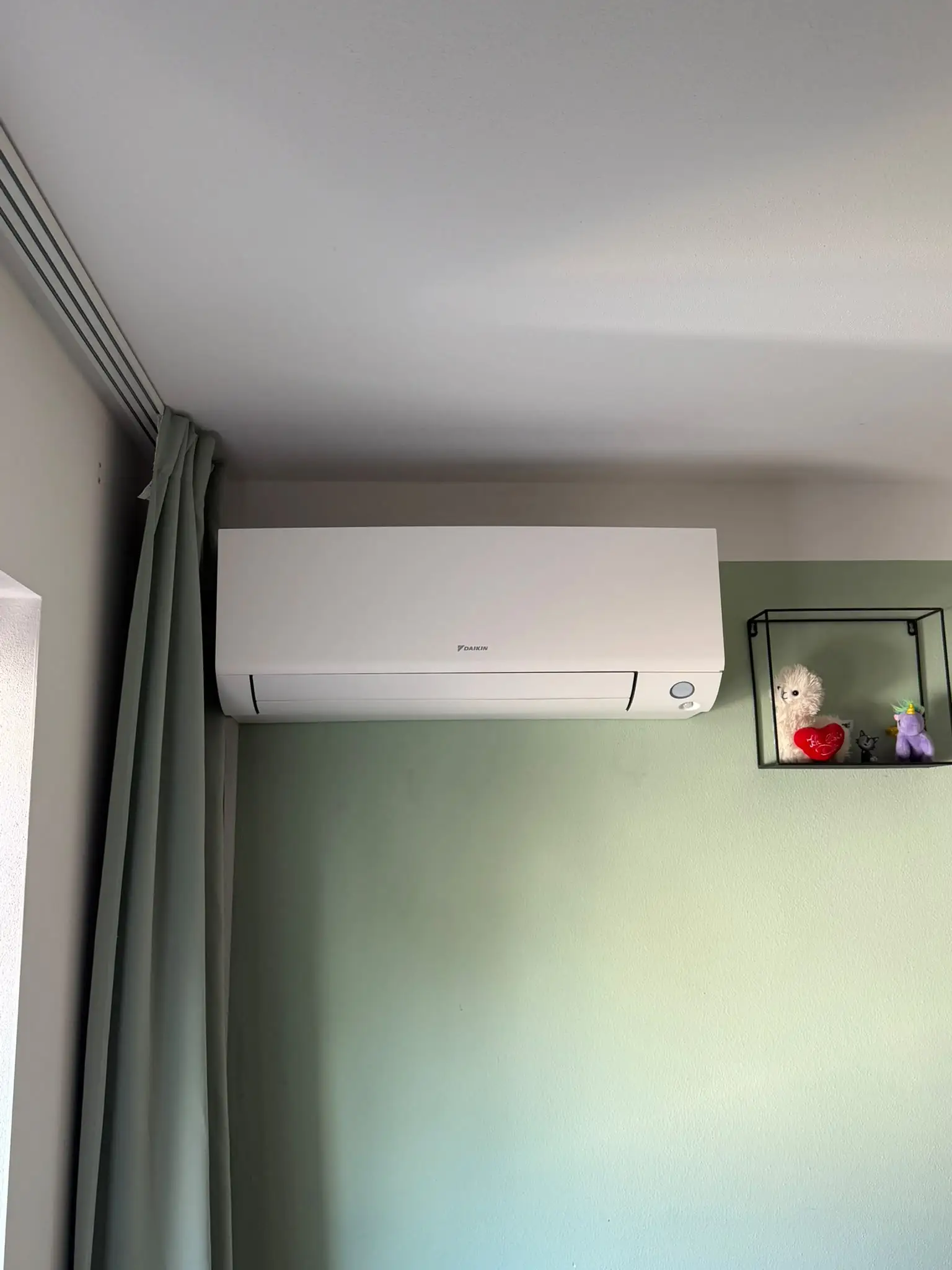 Innengerät von Daikin unter der Decke eines Wohnraums mit salbeigrüner Wand, direkt neben einer Vorhangschiene.