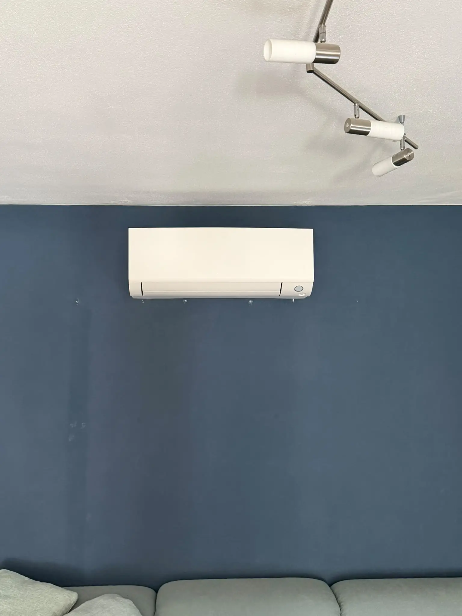 Weißes Innengerät einer Klimaanlage, dicht unter der Decke an einer dunkelblauen Wohnzimmerwand montiert.